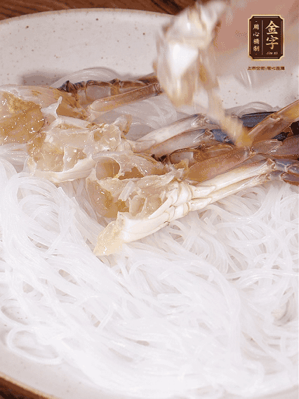 盤底墊上粉絲，擺上梭子蟹、火腿片，撒姜粒，淋上蒸魚豉油、花雕酒調(diào)味腌制15分鐘